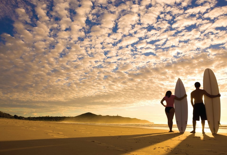 Two people standing with their surfboards on the beach at sunset in Melbourne, Australia.