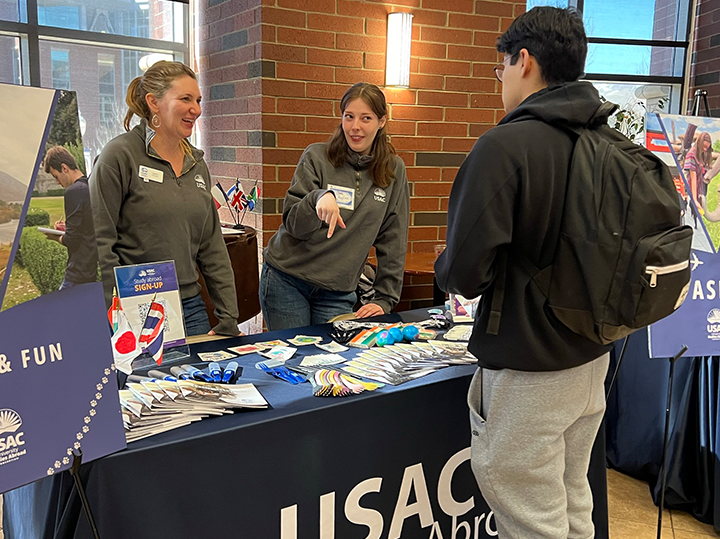 Two USAC employees at a tabling event talking to a student about studying abroad.