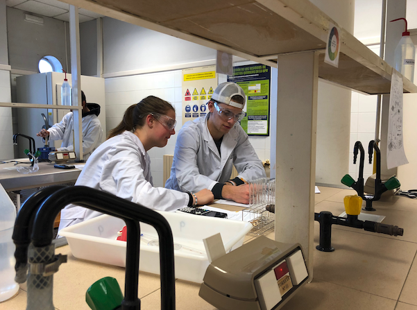 Two students standing in white lab coats and classes in a science lab at Universitat Politècnica de València in Valencia, Spain.