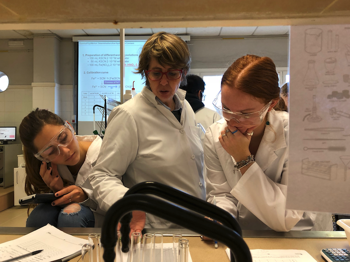 Two students standing next to a professor in white lab coats and classes in a science lab at Universitat Politècnica de València in Valencia, Spain.