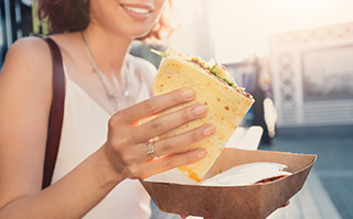 Woman standing outside holding a Greek gyro over a paper plate.