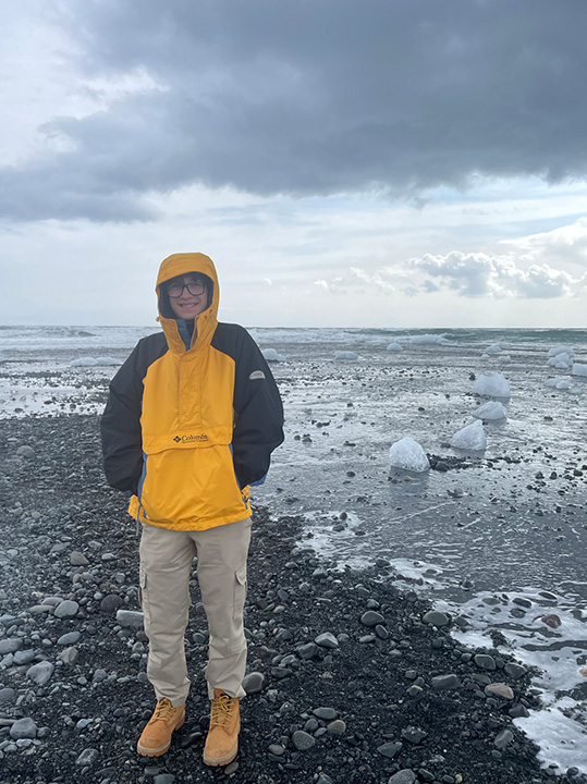 Trey Kirkpatrick in a yellow and black jacket with the sea and ice behind him in Iceland.