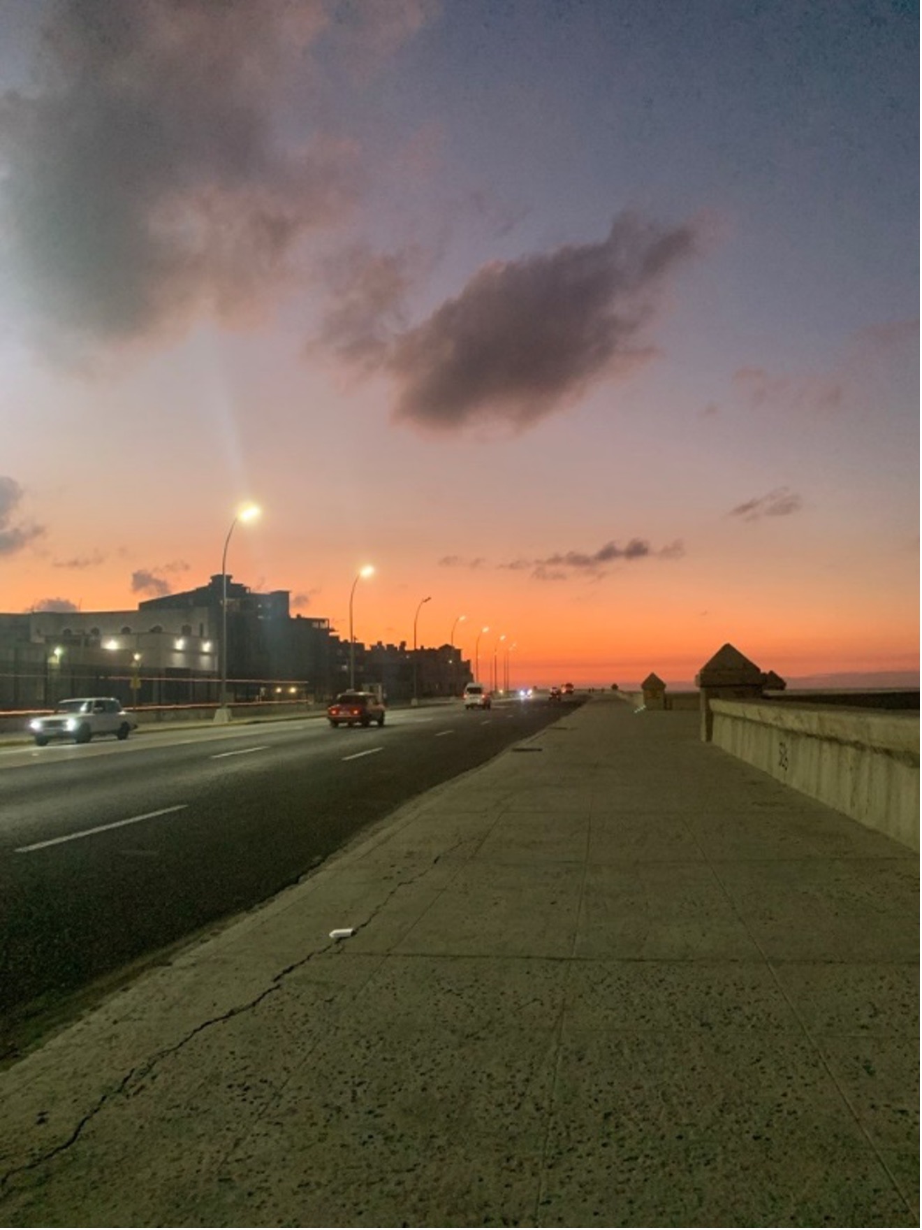 A sunset view of a walkway with vintage cars in La Habana, Cuba.