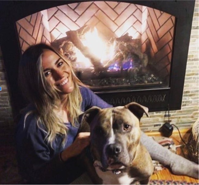 Kat Rogers sitting next to a fireplace with her dog.