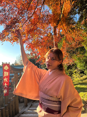 KayCee Carlen in a traditional Japanese kimono standing next to a tree with orange leaves in Nishinomiya, Japan.