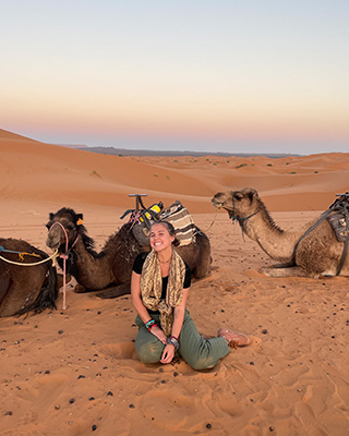 Mary Clingerman sitting in the desert with camels around her.