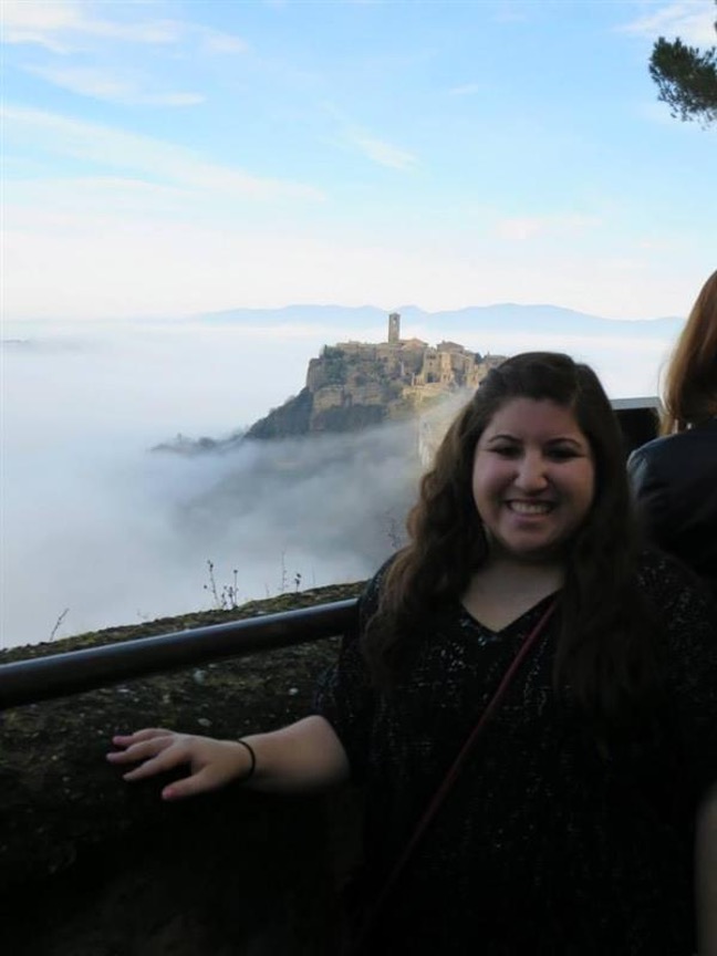 Rachel Alperstein standing next to a wall overlooking a castle in Italy.