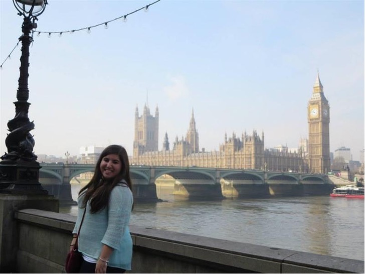 Rachel Alperstein standing next to the river with a view of the bridge and Parliament in the background in London, England..