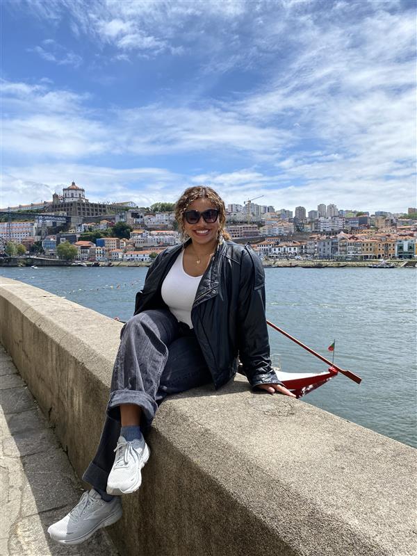 Josie sitting on a seawall with the sea and city in the background in Portugal.