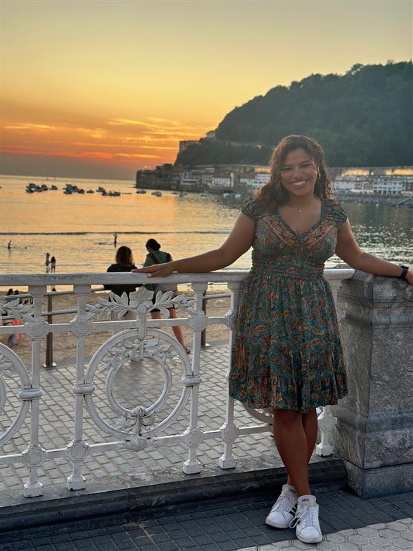 Josie posing next to the beach with a mountain and sunset in the background in San Sebastian, Spain.