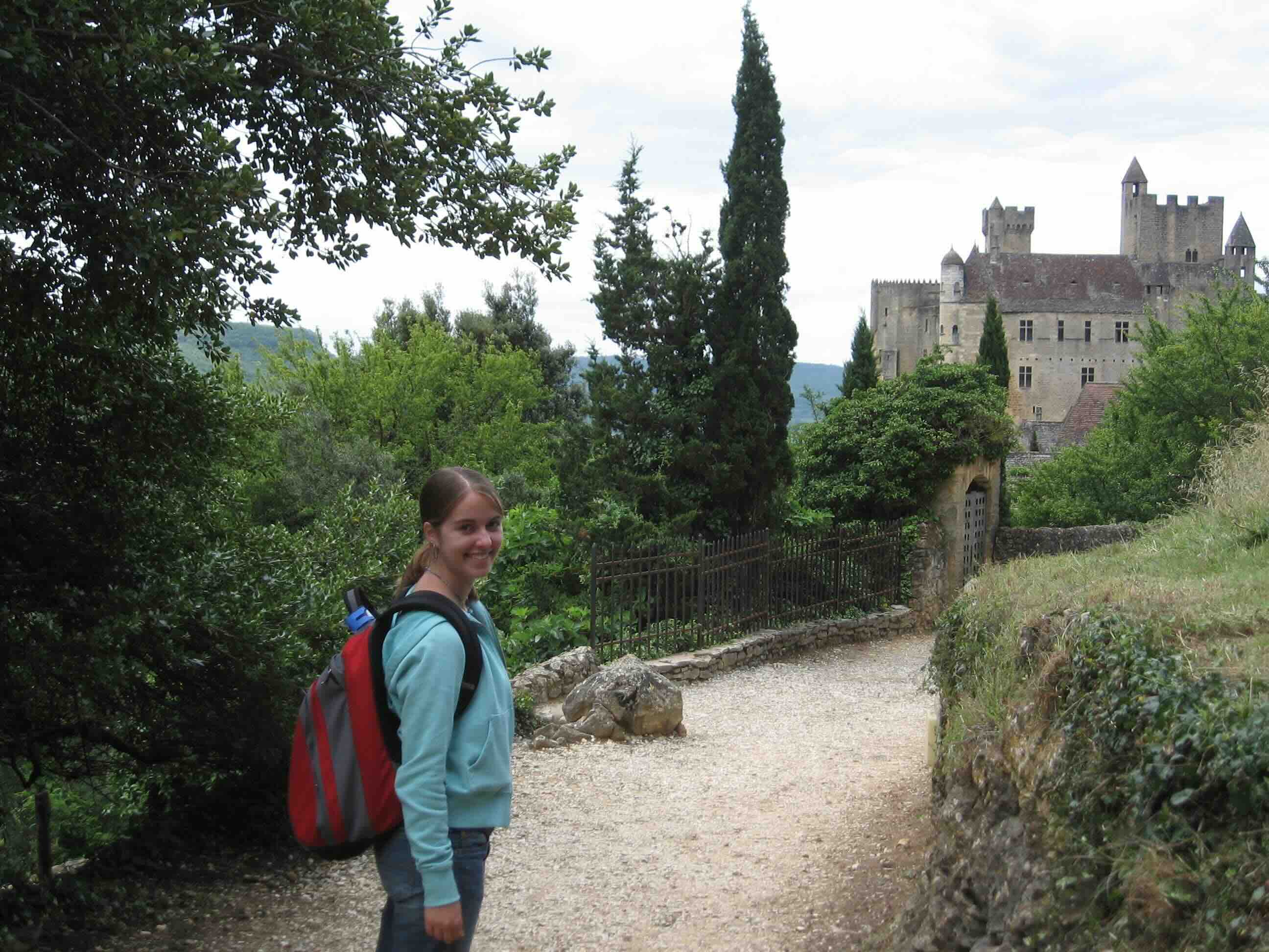 Katrina walking along a path with historic buildings in the background in Sarlat, France.