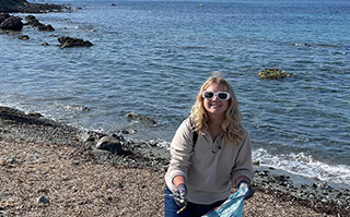 A student next to the ocean picking up trash on the beach in Alicante, Spain.