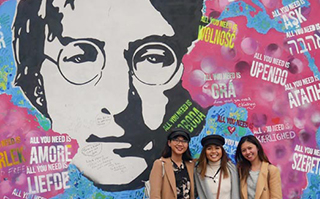 Three people posing in front of the John Lennon mural in Prague.