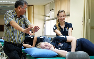 A teacher instructing a student in a health class with another student laying on a table.
