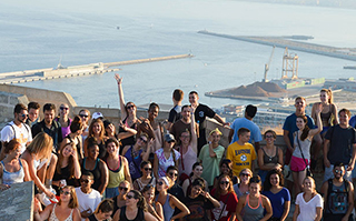 A large group of people standing at the top of a lookout with the ocean in the background.