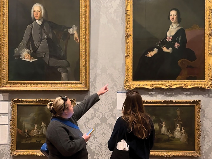 Two people admiring framed portraits at a museum.