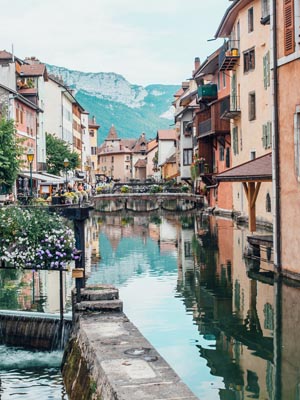 View of a canal with historic buildings with mountains in the background in France.