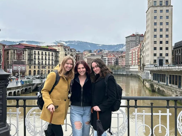 Three friends posing together with a river and buildings in the background in Bilbao, Spain.