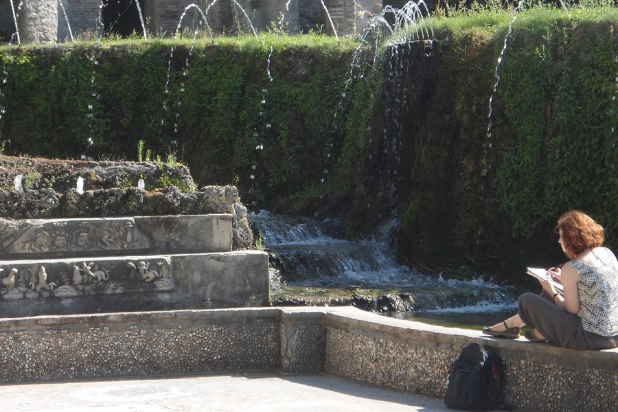 A student sitting reading by a fountain.