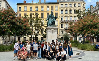 A group of students in front of a statue and historic buildings in Lyon, France.