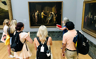 A group of students and a professor at a museum studying a painting in London, England.