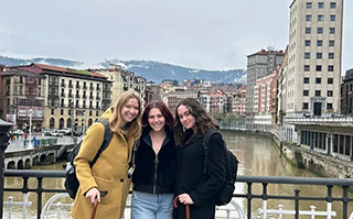 Three students on a bridge overlooking the river and historic buildings in Bilbao, Spain.