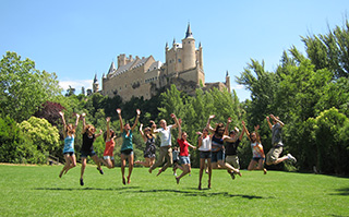 Students jumping together on the grass in front of a castle in Madrid, Spain.