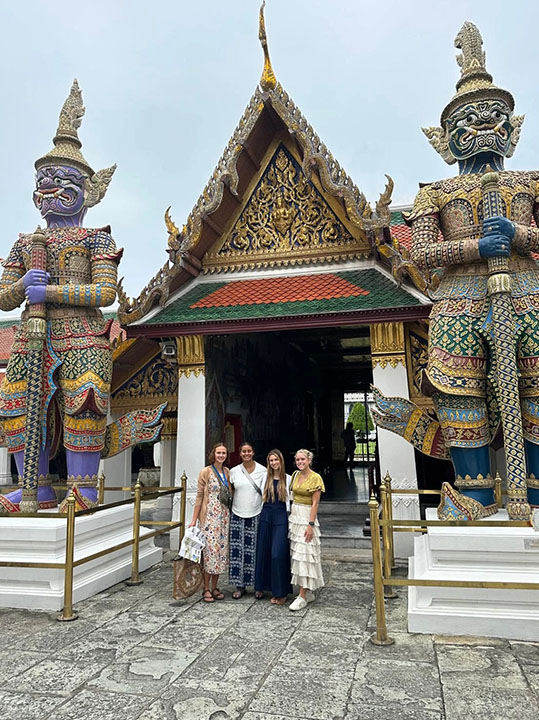 Four students standing in front of a traditional Thai Wat in Khon Kaen, Thailand.