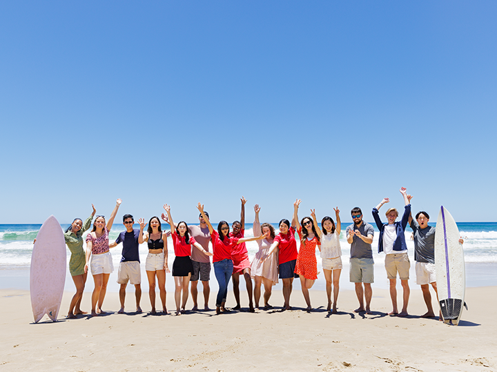 A group of students with their hands in the air on the beach in Gold Coast, Australia. 