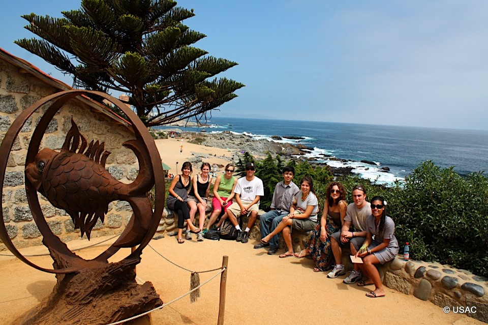 Students sitting in next to a statue in Isla Negra with a view of the ocean behind.