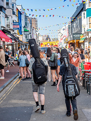 Students walking a busy pedestrian area with guitars on their backs in Brighton, England.