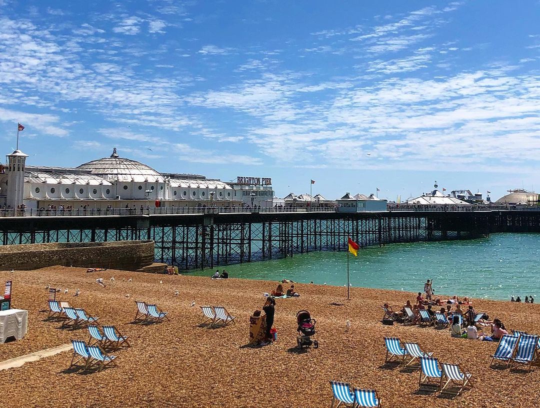 A beach with chairs and people with the Brighton Pier in the background in Brighton, England.