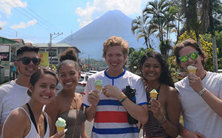 A group of people eating ice cream outside with palm trees and a mountain in the background in Heredia, Costa Rica.