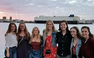 A group of people standing together with the ocean and a port in the background in Auckland, New Zealand.