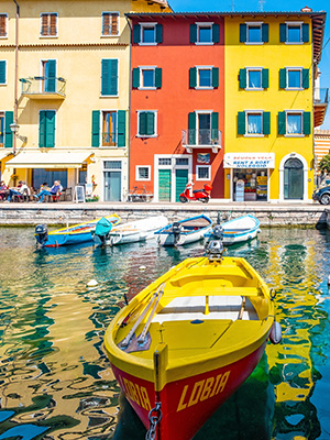 A yellow boat in Lake Garda in front of colorful buildings in Sirmione, Italy.