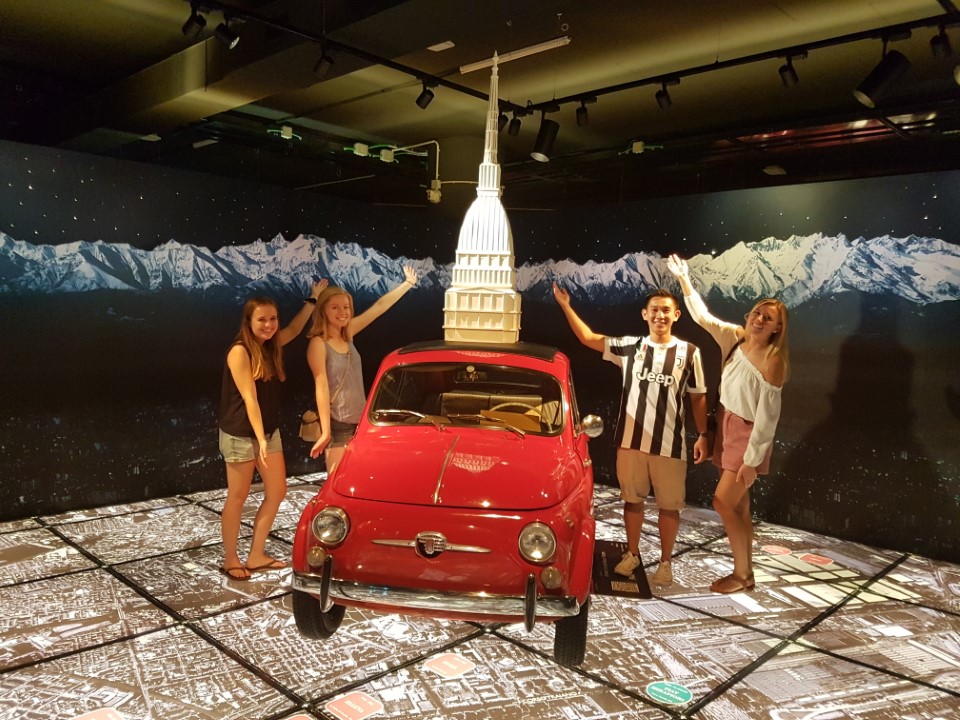 Four people posing next to a red FIAT car in the National Automobile Museum in Italy.