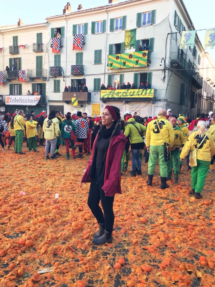 A woman surrounded by oranges on the ground having fun at the Ivrea Festival in Italy.