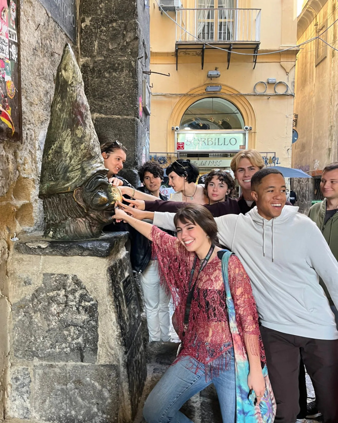 Students on Naples street touching the Busto di Pulcinella in Naples, Italy.