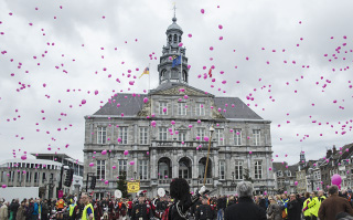A group of people gathered in front of a historic building with pink balloons floating above them in Maastricht, Netherlands.