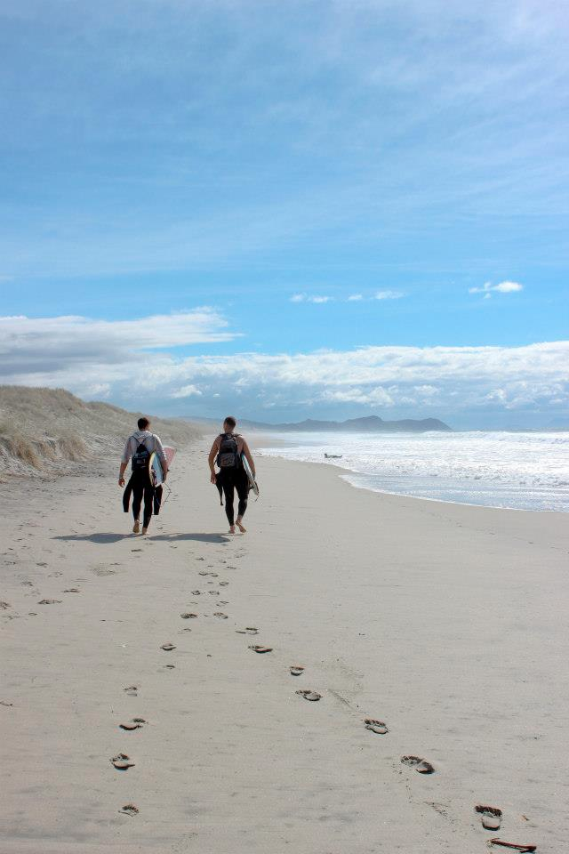 Two surfers walking along the beach in Auckland, New Zealand.
