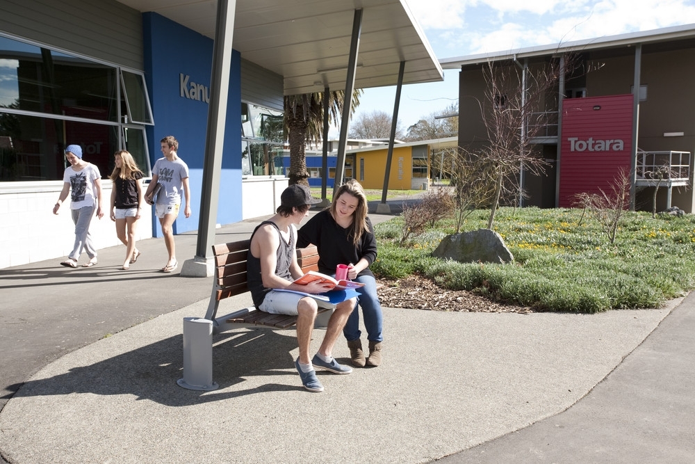 Students sitting on a bench outside Matai Hall on the Manawatu Campus of Massey University in Palmerston North, New Zealand.