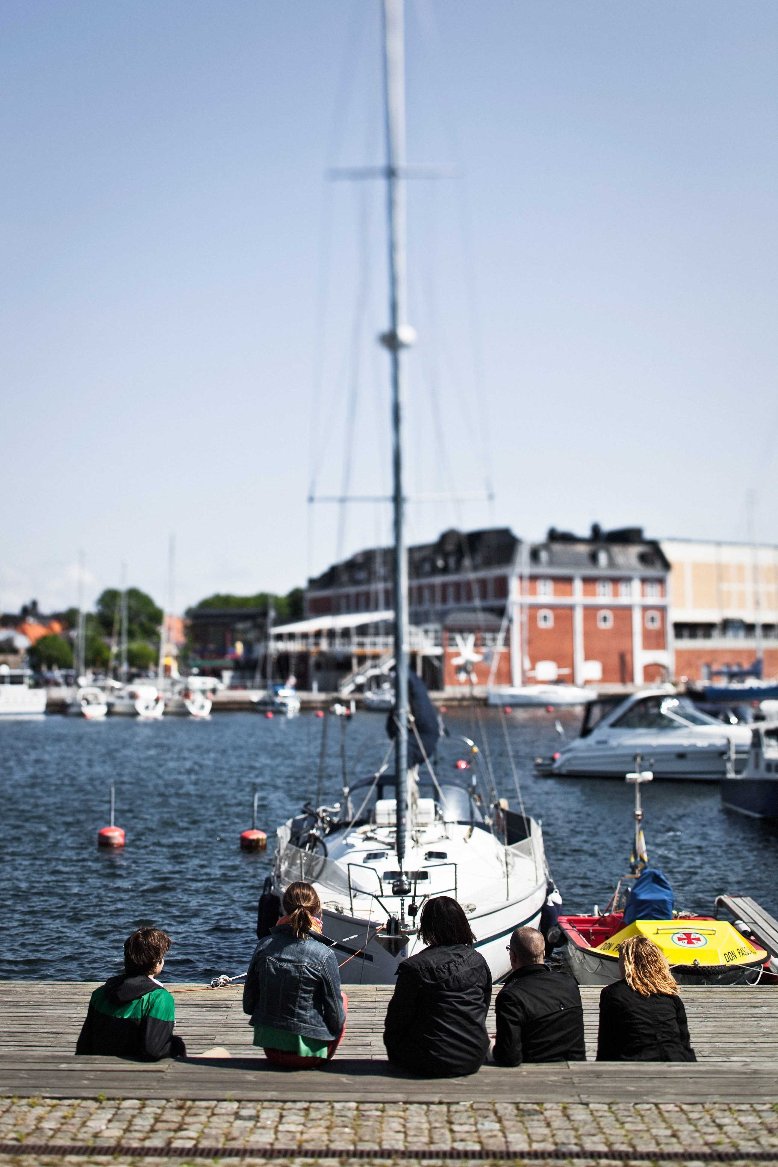 People sitting on the dock with a sailboat in front of them in Växjö, Sweden.