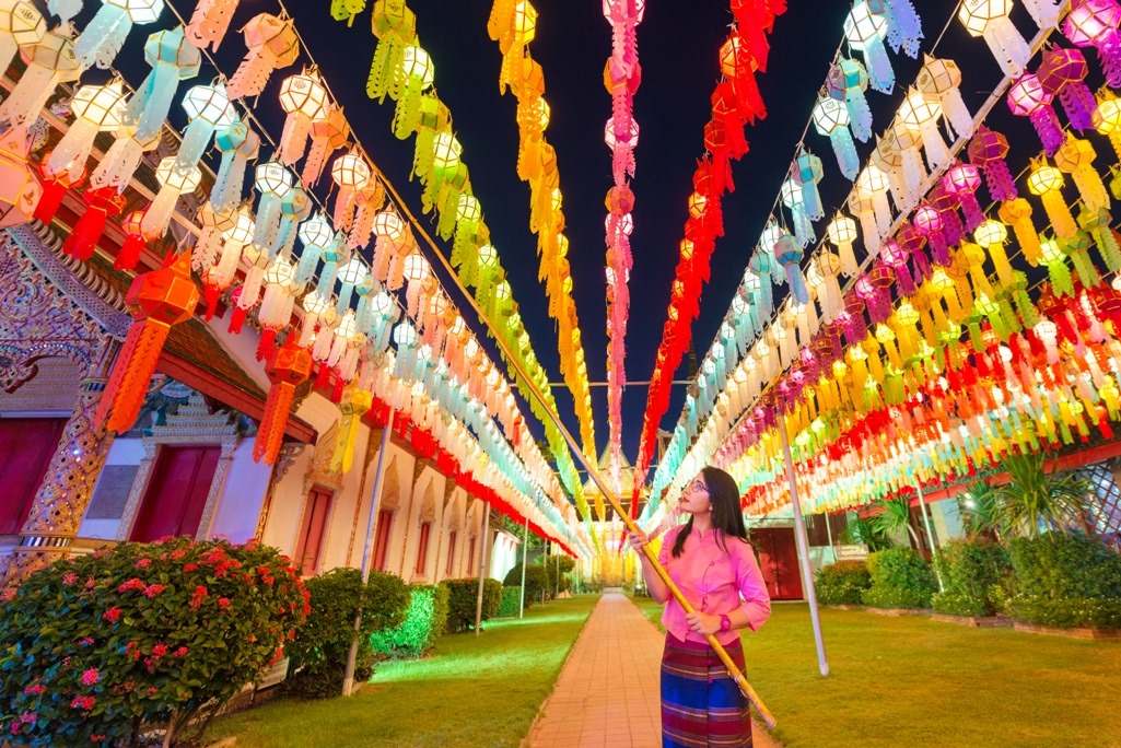 Woman standing below thousands of colorful Thai lanterns lit up at night at the Lamphun Hundred Thousands Lantern Festival in Thailand.