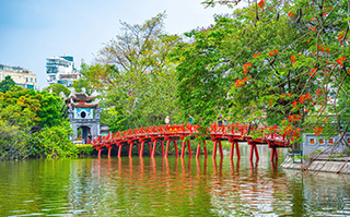 A red bridge over Hoan Kiem Lake with the city in the background in Hanoi, Vietnam.