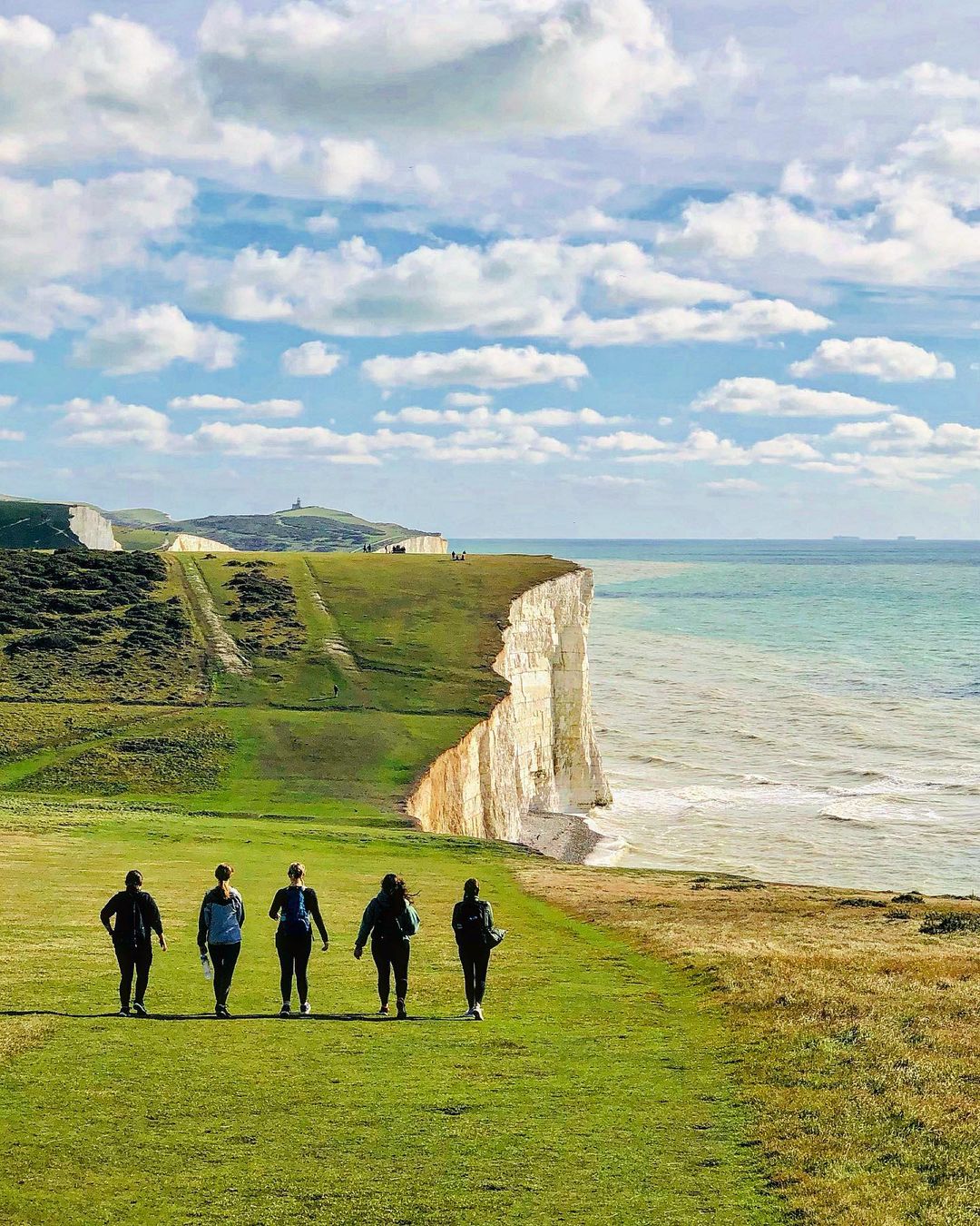 Five people walking on a grassy area on the Seven Sisters hike overlooking the cliffs and ocean.